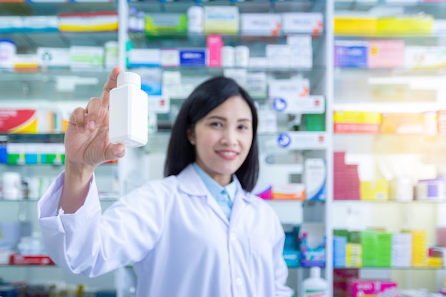 De hand van de apotheker die de medicijnfles vasthoudt met de wazige achtergrond van de apotheekplanken.