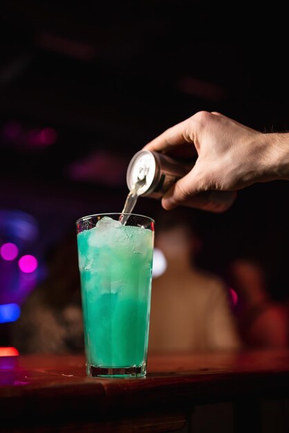 De hand van de barman giet water in een zomerse koude blauwe lagunecocktail met likeurijsblokjes