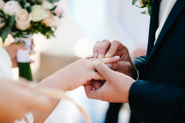 De hand van de bruidegom draagt een gouden verlovingsring om de vinger van de bruid. Trouwdag. Handen met trouwringen. Detailopname.