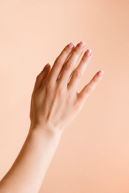 De hand van de gemanicuurde vrouw op bleke oranje achtergrond
