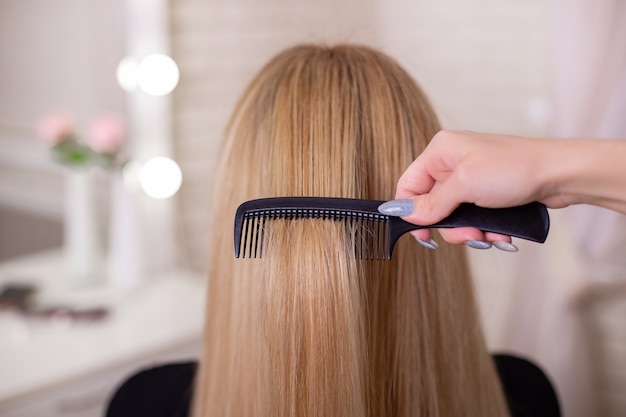 De hand van de kapper die lang natuurlijk blond haar borstelt