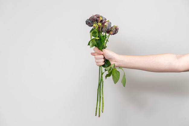 De hand van de man houdt een boeket verwelkte bloemen voor en toont een vijg