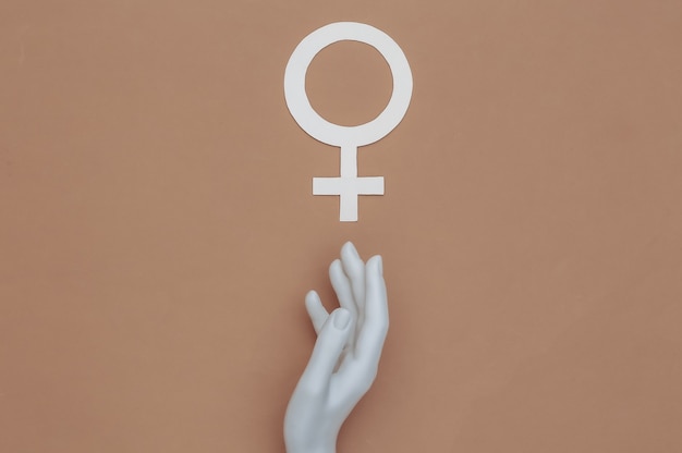 Foto de hand van de mannequin raakt het symbool van het vrouwelijke geslacht op een bruine achtergrond. bovenaanzicht