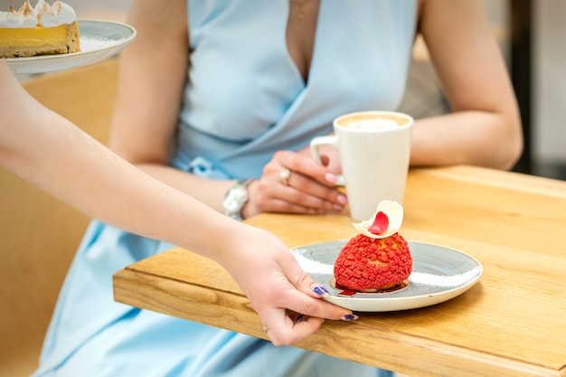 De hand van de ober legt op de tafel een bord met een rode cupcake op de achtergrond van een vrouwelijke klant in een café