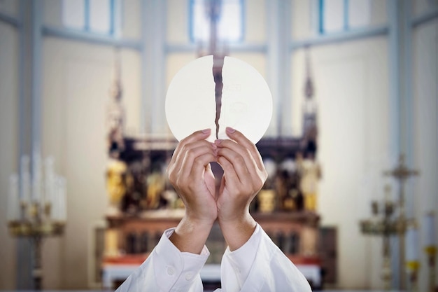 De hand van de pastoor breekt het communiebrood in de kerk