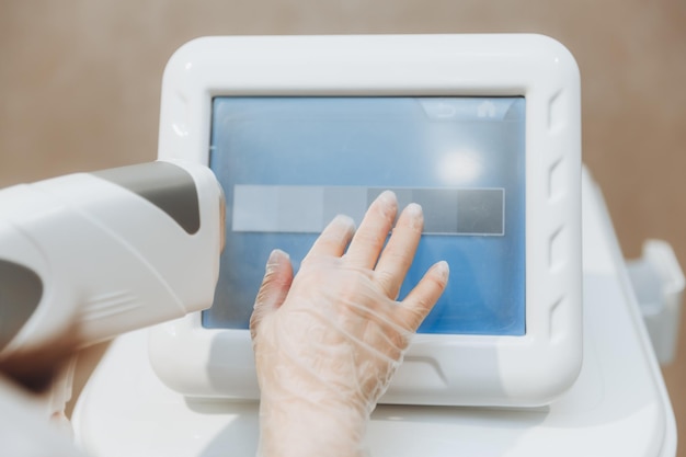 De hand van de schoonheidsspecialiste drukt op de knoppen op het apparaat voor laserontharing Close-up Huidverzorgingsapparatuur