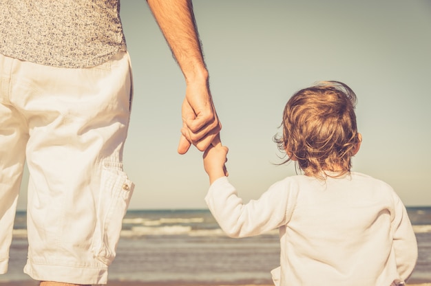 De hand van de vader leidt zijn kindzoon in de aard van het de zomerstrand openlucht, vertrouwt familieconcept