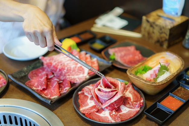 De hand van de vrouw gebruikt een tang om Wagyu-rundvlees op een bord te leggen, klaar om boven houtskool te grillen