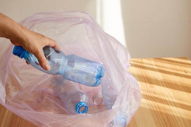 Foto de hand van de vrouw gooit een plastic fles in een vuilniszak