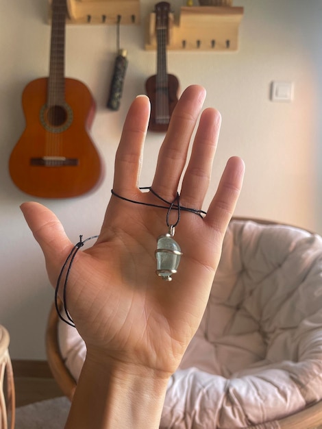 De hand van de vrouw houdt een hanger van fluorietsteen vast met een gitaar en een ukelele die aan de muur hangt