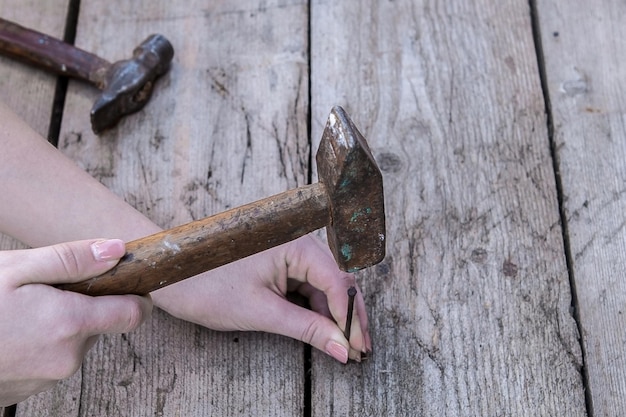 De hand van de vrouw is een hamer en om een spijker te slaan ligt op een zwarte houten tafel Kopieer de ruimte