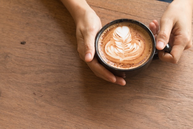 De hand van de vrouw is het houden van Piccolo Latte kunst in een beker topping mooie hartkunst uit melk