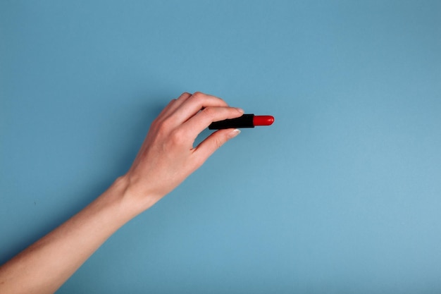 De hand van de vrouw neemt rode lippenstift geïsoleerd op de blauwe achtergrond