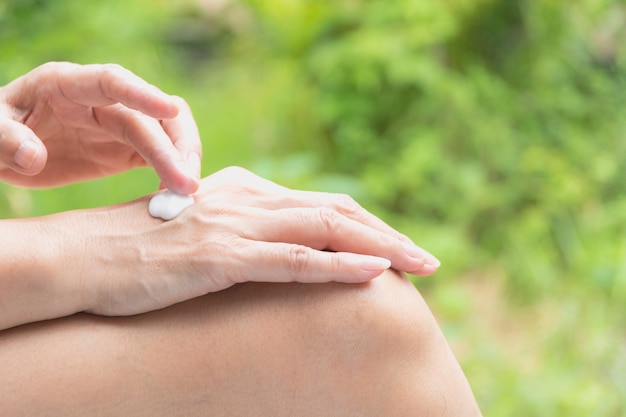 de hand van de vrouw past lotion op de huid van de rug hand op de natuur achtergrond.