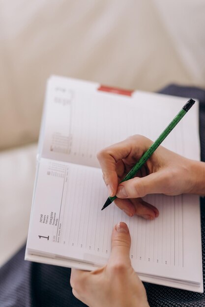 De hand van de vrouw schrijft op een spiraalvormig boek op de tafel De handen van het meisje schrijven in het dagboek