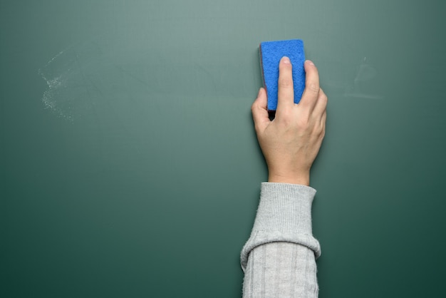 De hand van de vrouw veegt een groen krijtbord af met een blauwe spons, close-up