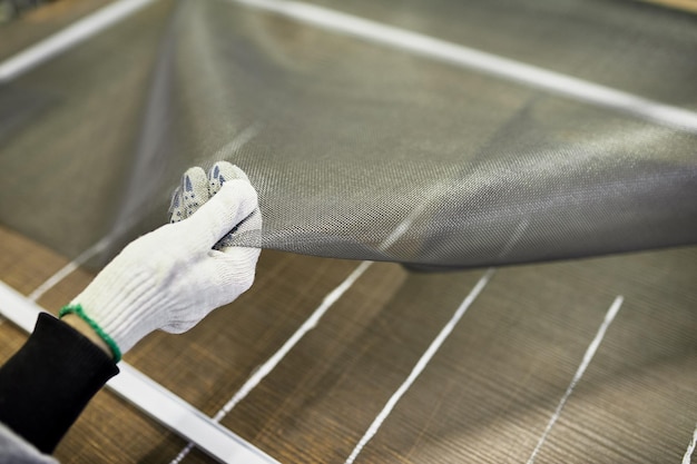 Foto de hand van een arbeider, verzamelt panelen om te beschermen tegen insecten, houdt een klamboe voor ramen vast