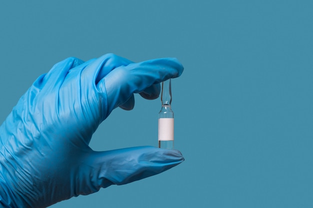 De hand van een arts in een blauwe handschoen houdt een fles covid-19-medicijn of vaccin vast op een blauwe achtergrond. vloeibaar medicijn, tegengif voor het virus