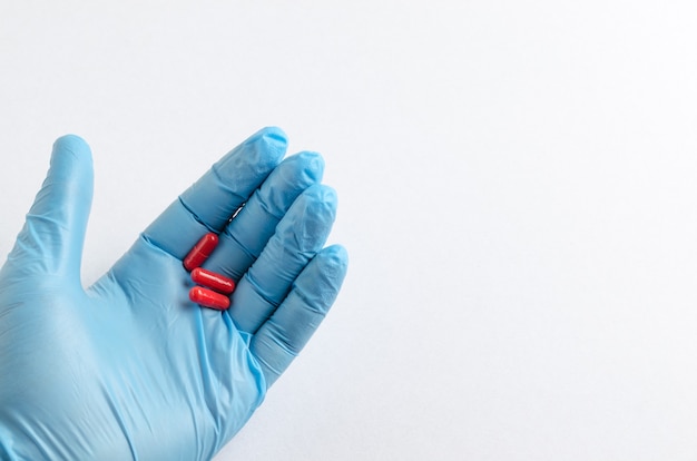 De hand van een gezondheidswerker in blauwe medische handschoenen met een pil