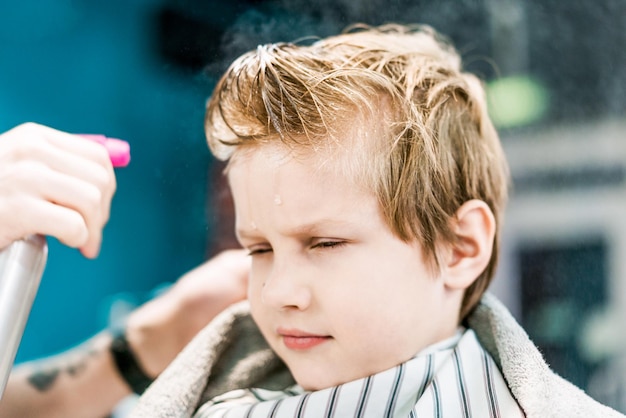 De hand van een kapper spat het water op het hoofd van de jongen