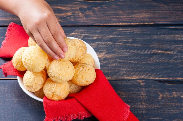 De hand van een kind die een Braziliaans kaasbrood oppakt. Ook bekend in Latijns-Amerika als Chipa, Pan de Bono en Pan de Yuca.