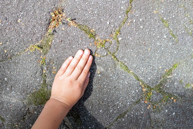 De hand van een kind die iets bedekt op een oud asfaltoppervlak