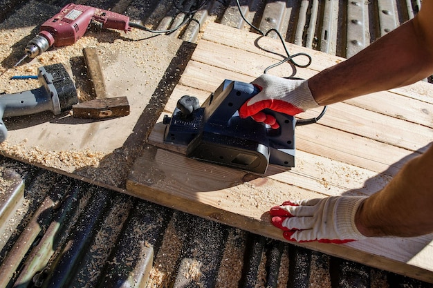 De hand van een man die werkt met een elektrische schaafmachine en geschaafde planken