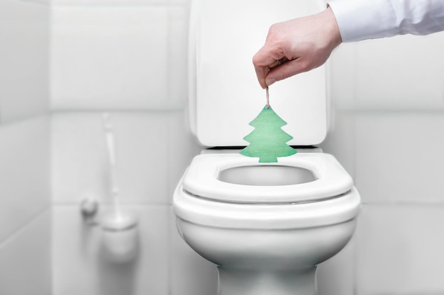 De hand van een man gooit een kerstboom in het toiletsymbool van het einde van de kerst en het nieuwe jaar...