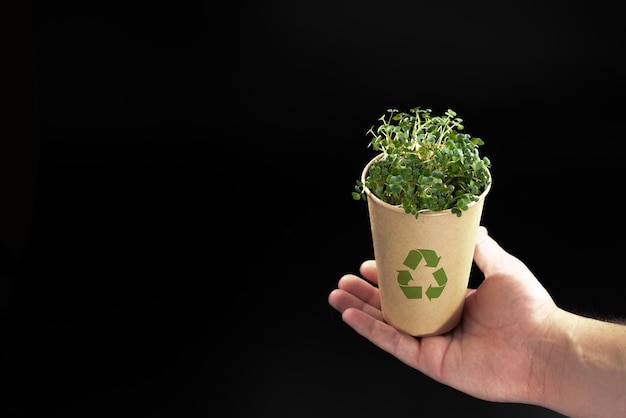 De hand van een man houdt een kraftbeker met groen vast in het concept van het recyclen van het leven zonder plastic