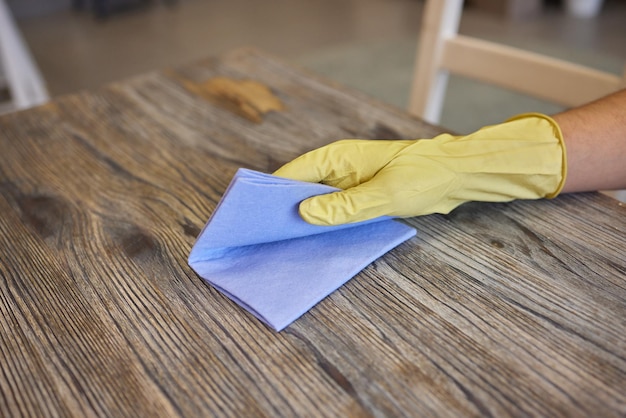 De hand van een man in een medische handschoen veegt de tafel af met servet Achtergrondkelner in een schort in onscherpte Oppervlaktebehandeling