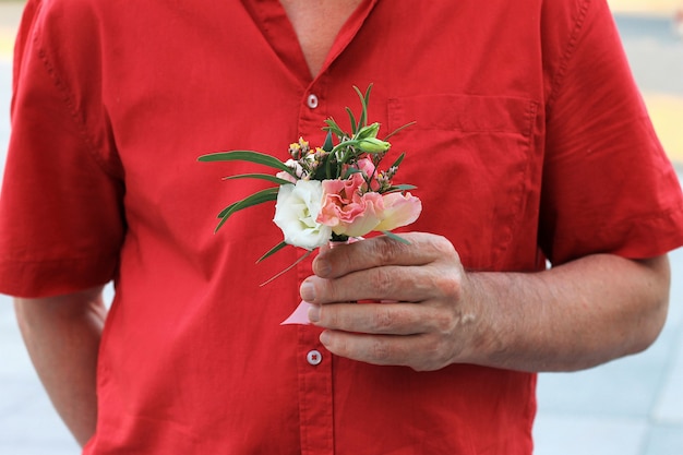 De hand van een man in een rood shirt houdt een klein mooi boeket vast