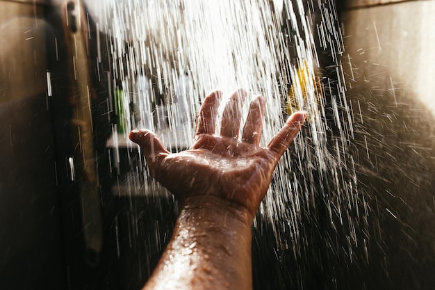 De hand van een man in een spray van water in het zonlicht tegen een donkere achtergrond.