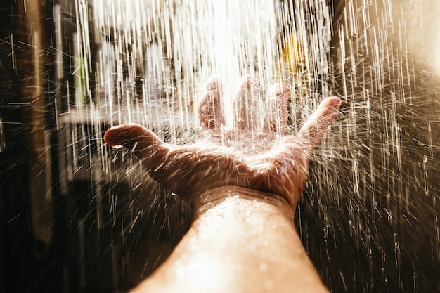 De hand van een man in een spray van water in het zonlicht tegen een donkere achtergrond.