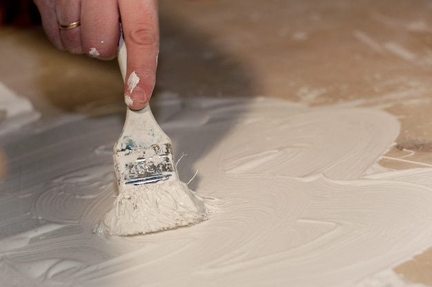 De hand van een man schildert het oppervlak met een witte kwast