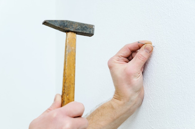 Foto de hand van een man steekt een spijker in de muur om een schilderij op te hangen