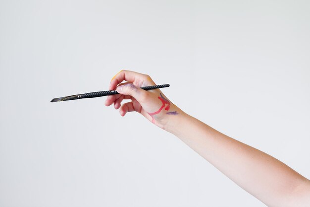 De hand van een meisjeskunstenaar houdt een penseel vast om op een witte achtergrond te schilderen