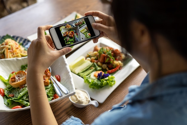 Foto de hand van een vrouw die een smartphone gebruikt om een lunch of diner in een restaurant te fotograferen.
