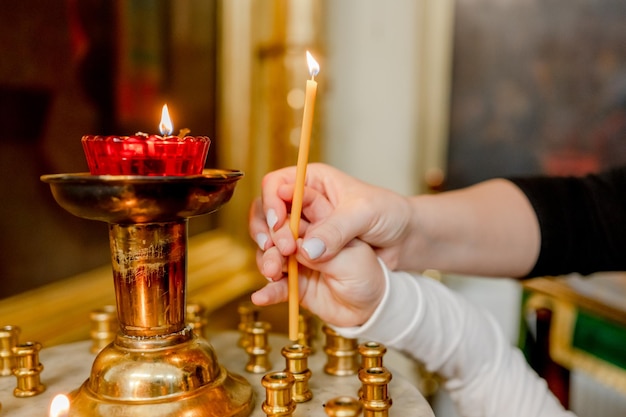 De hand van een vrouw en een kind zetten een kaars in de kerk