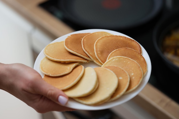 De hand van een vrouw houdt een bord pannenkoeken vast, close-up. Huisgemaakt vers gebak voor ontbijt, traditionele lunch