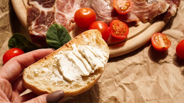 De hand van een vrouw houdt een bruschetta en spreidt kwark uit