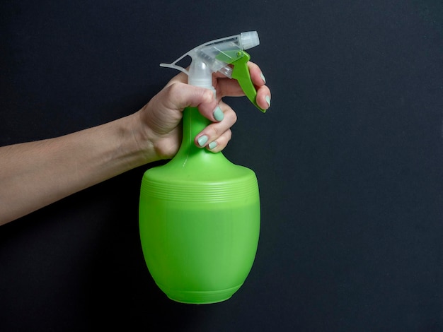De hand van een vrouw houdt een plastic fles vast met een groene spuitfles op een donkere achtergrond. Het concept van thuiszorg en schoonmaak.
