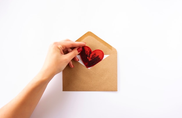 De hand van een vrouw houdt een rood hart in een bruine envelop