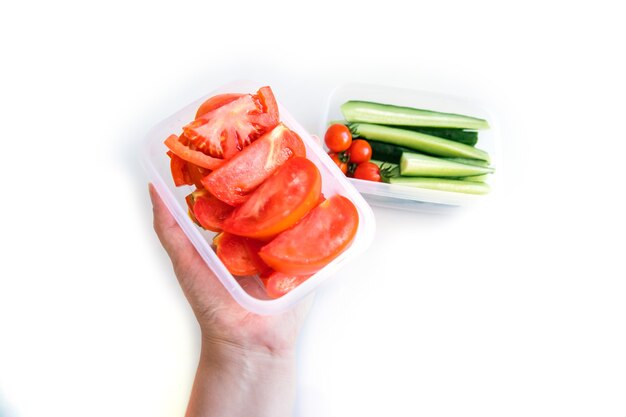 De hand van een vrouw houdt gesneden groenten vast in een plastic container op een witte achtergrond.