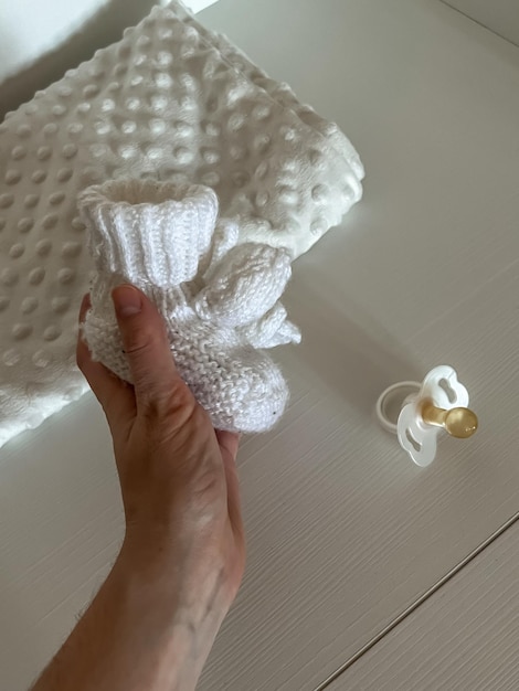 Foto de hand van een vrouw houdt kleine gebreide kindersokken wit tegen een achtergrond van tepels en een witte ruit