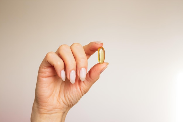 de hand van een vrouw houdt met haar vingers een zachte gele gelcapsule close-up vast op een beige achtergrond