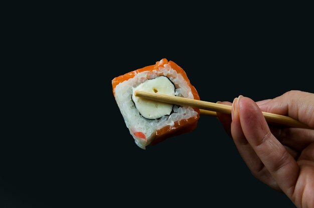 De hand van een vrouw houdt sushi vast met houten stokken close-up