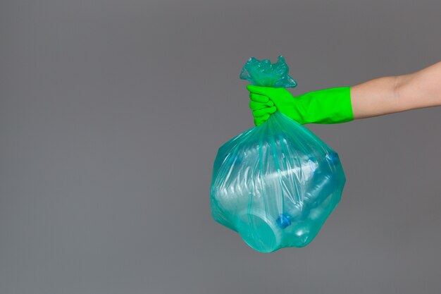 De hand van een vrouw in een rubberhandschoen houdt een transparante groene vuilniszak