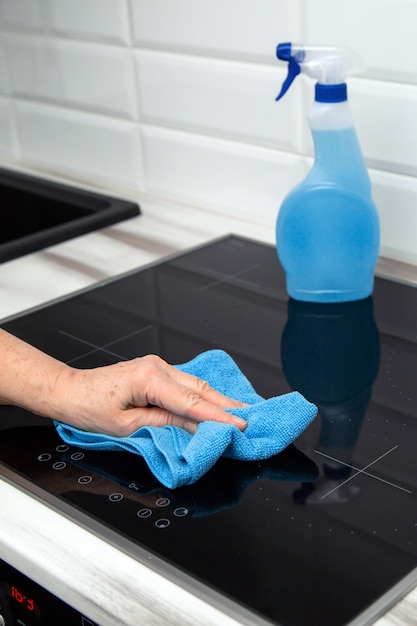 De hand van een vrouw met een blauwe microvezeldoek wrijft over een keramische plaat in de keuken.