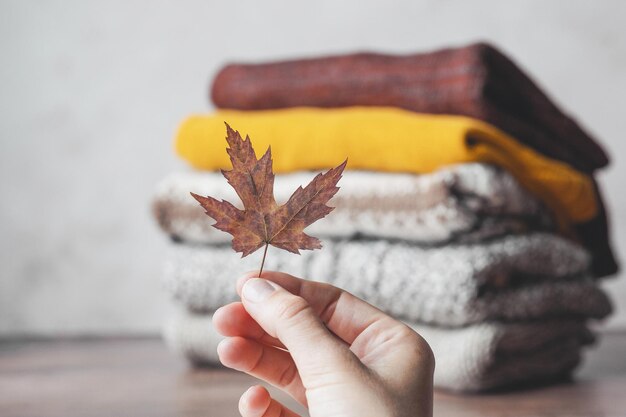 De hand van een vrouw met een gevallen blad op de achtergrond van een stapel gebreide truien.