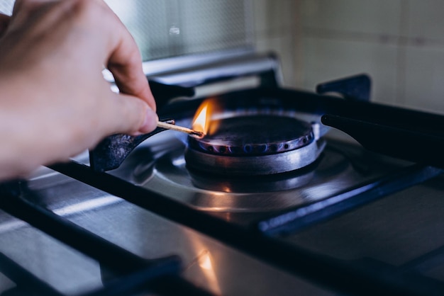 De hand van een vrouw met een lucifer steekt het gasfornuis aan in haar appartement